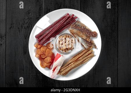 Getrocknete Calamari, Fisch, Kaviarstäbchen, Krabbensurimi, gesalzene Erdnüsse auf dem Teller Stockfoto