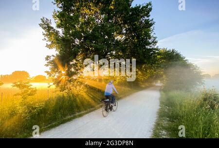 Laatzen, Deutschland. Juni 2021. Ein Mann fährt bei Sonnenaufgang um 5:40 Uhr mit dem Fahrrad und leichtem Bodennebel durch die Leinemesch in der Region Hannover. Der Deutsche Wetterdienst DWD prognostiziert für die nächsten Tage eine Hitzewelle mit Temperaturen bis zu 37 Grad. Quelle: Julian Stratenschulte/dpa/Alamy Live News Stockfoto