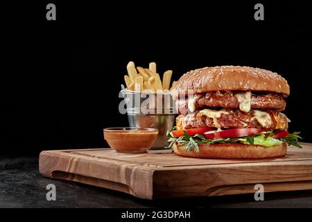 Double Burger mit Pommes und Sauce auf Holzbrett Stockfoto