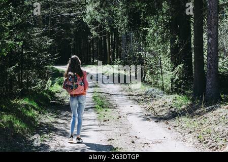 Ein junges Mädchen mit Rucksack zu Fuß entlang Weg durch den Wald während des Sommers. Hipster Lifestyle und Solo Trip.Rückansicht. Stockfoto