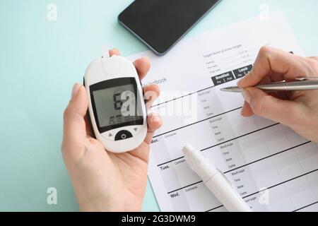 Person hält Glucometer mit Blutzuckermesswerten und macht Notizen im Notizbuch Stockfoto