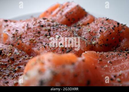 Appetitliche Stücke frischen rohen Lachses mit Gewürzen darauf liegen Eine weiße Platte Stockfoto