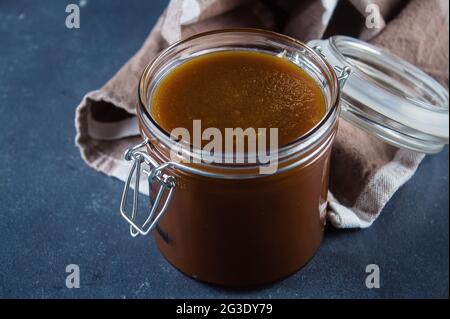 Hausgemachte gesalzene Karamellsauce im Glas auf blauem Beton-Tischhintergrund. Speicherplatz kopieren Stockfoto
