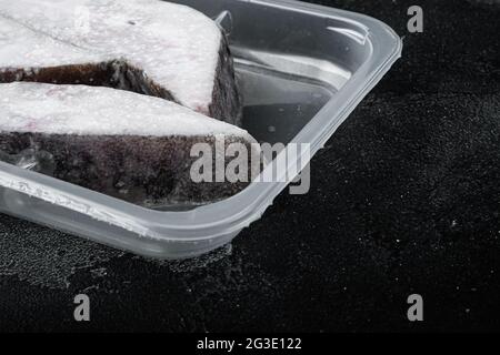 Tiefkühlset für grönländische Heilbutt-Steaks, auf schwarzem Tischhintergrund aus dunklem Stein, mit Platz für Text Stockfoto