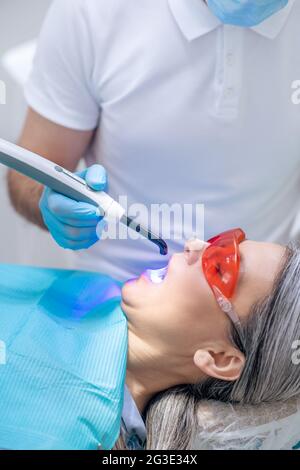 Frau in einer Schutzbrille, die eine Zahnrestauration im Zahnarztbüro hat Stockfoto