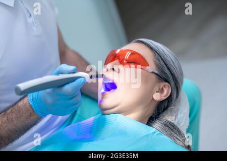 Frau in einer Schutzbrille, die eine Zahnrestauration im Zahnarztbüro hat Stockfoto