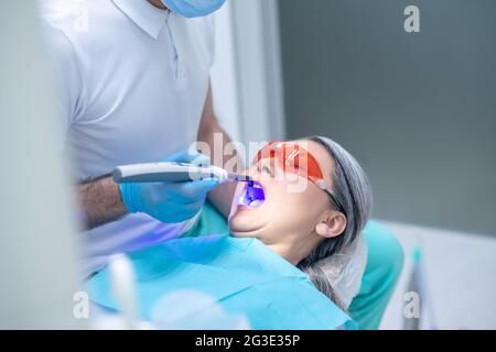 Frau in einer Schutzbrille, die eine Zahnrestauration im Zahnarztbüro hat Stockfoto