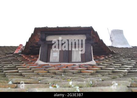 Kleines Dachfenster auf dem Ziegeldach eines alten Gebäudes und Kamin Stockfoto