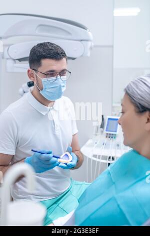 Junger Zahnarzt, der seiner Patientin eine Prothese zeigt Stockfoto