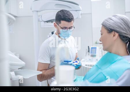 Junger Zahnarzt, der seiner Patientin eine Prothese zeigt Stockfoto
