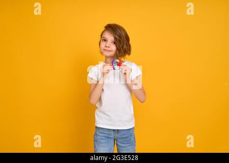 Kleines Mädchen hält Pop it Antistress-Spielzeug auf gelbem Hintergrund Stockfoto