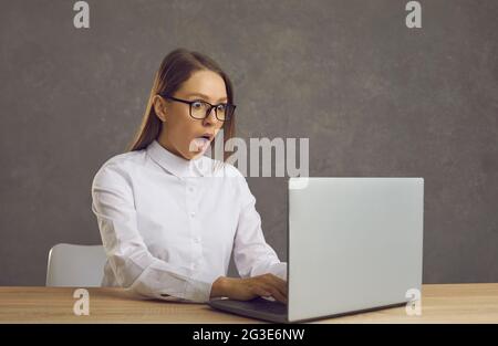 Porträt einer jungen, schockierten, erstaunten Geschäftsfrau, die am Laptop arbeitet Stockfoto