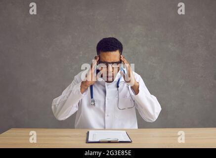 Schockierter junger afroamerikanischer Arzt greift sich den Kopf, während er Informationen aus dem Clipboard liest. Stockfoto