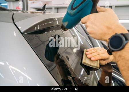 Der professionelle Detailer wärmt die Tönfolie mit einem Industrietrockner auf, um Tönungen auf Autoglas aus nächster Nähe zu auftragen. Stockfoto