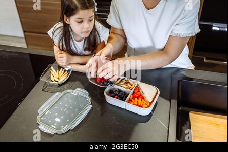 Mädchen beobachten ihre Mutter Lebensmittel in ihre Lunchbox Stockfoto