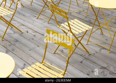 Gelbe Bistrostühle und -Tische auf einer Holzterrasse. Stockfoto