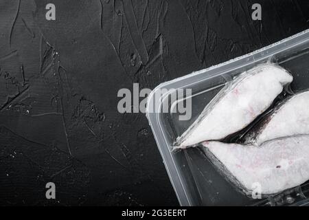 Tiefkühlset für grönländische Heilbutt-Steaks, auf schwarzem dunklen Steintisch-Hintergrund, Draufsicht flach liegend, mit Platz für Text Stockfoto