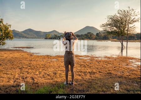 Junge asiatische Frau, die im Sonnenuntergang ein Foto mit dem Smartphone am Bergsee gemacht hat Stockfoto