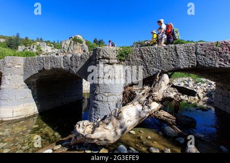 FRANKREICH. ARDECHE (07) LABEAUME VILLAGE DE CARACTERE (CHARAKTERLICHES DORF) EIN BAUMSTAMM, DER UNTER DER SINKBAREN BRÜCKE EINGEKEILT IST, EINE GRUPPE VON WANDERERN Stockfoto