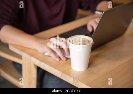 Freiberuflicher Mann, der mit einem Laptop und einer Kaffeetasse auf einem Holztisch im Café arbeitet Stockfoto
