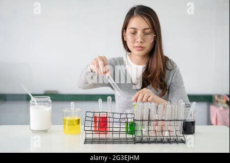 Junge Studentin asiatische Frau Herstellung Analyse und Mischen von Flüssigkeit in Reagenzglas, Farbbecher im Experimentlabor in der Wissenschaft Klasse Stockfoto