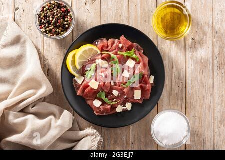 Carpacio aus marmortem Rindfleisch auf schwarzem Teller und rustikalem Holztisch Stockfoto