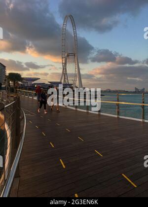 Wunderschöne Aussicht auf Touristen, die bei Sonnenuntergang auf der Brücke spazieren und Ain Dubai im Hintergrund. Stockfoto