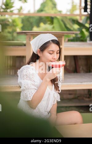 Schöne junge asiatische Frau, die im Sommer im Café gemischte Beerenmocktail trinkt Stockfoto