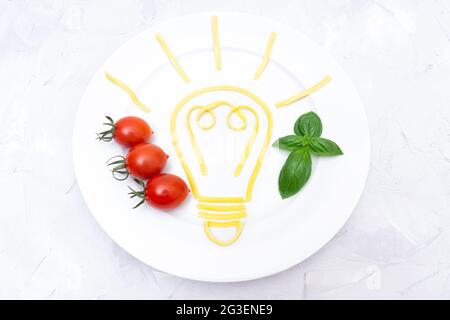 Zutaten für ein neues Rezept: Frische Kochidee in Form einer glühenden Glühbirne aus gekochter Pasta auf weißem Teller Stockfoto