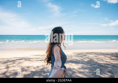 Schöne junge asiatische Frau hält Hände mit Freund am Strand im tropischen Meer im Urlaub. Sommer- und Urlaubskonzept Stockfoto