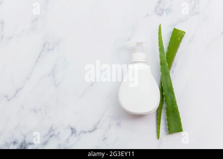 Aloe Vera natürliche Hautpflege weiße Produktflasche mit grünen Blättern. Flache Lay-Komposition Stockfoto