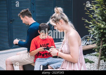 Moderne junge Familie mit moderner Technik.beim Spaziergang auf dem Stadtplatz schaut jeder auf sein Smartphone oder Tablet.Sie fühlen sich nicht von jedem angezogen Stockfoto