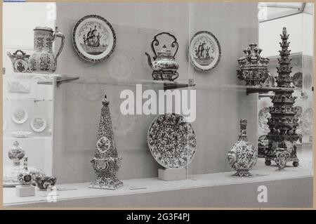 Vitrine mit Keramikoobjekten, darunter Obelisk, Komfoor und Blumenhalter; Vitters stellt Kunsthandwerk her. Dies ist das Gerät der Vitrine vor der Entleerung im Oktober 1959. Links am Boden eines Obelisken, geschmückt mit Blumen und Medaillons, in denen sitzende und stehende Frauenfiguren, in der Delfter Plateelbakkerij den Metalltopf hergestellt haben. Extrem rechts EINE Blütenpyramide aus Delfter Steingut, von einem anonymen Hersteller. Oben in der Mitte ein Kessel auf Komfoor, bemalt mit Blumen und Vögeln im Garten, von einem anonymen Delfter Hersteller. Stockfoto