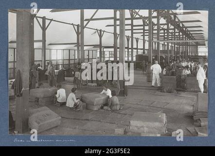 Indische Männer und Frauen, die in einem Schuppen auf Sumatra mit dem Pressen und Nähen von Tabakpackungen beschäftigt sind. Teil des Reisealbums mit Fotos von Aktivitäten und Sehenswürdigkeiten auf Sumatra und Java und von der Reise nach und von den Niederländischen Ostindien. Stockfoto