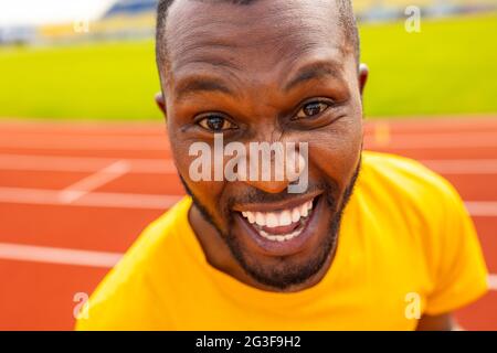Nahaufnahme des jungen sportlichen afroamerikanischen schwarzen Sportmanns in gelber Sportkleidung, der die Kamera anschaut und unbeschwert und aufgeregt jubelt, nachdem er erfolgreich war Stockfoto