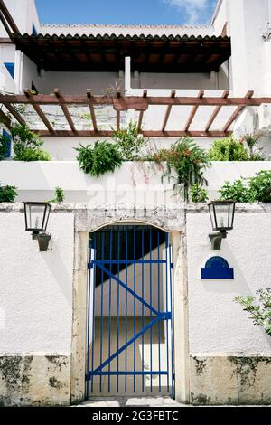 Steinzaun mit Gittertoren in der Nähe des Hauses mit einem großen Balkon und viel Grün Stockfoto