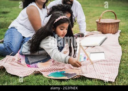 Indische Eltern, die Spaß haben, mit Kindern im Freien im Stadtpark zu malen - Hauptfokus auf Mädchengesicht Stockfoto