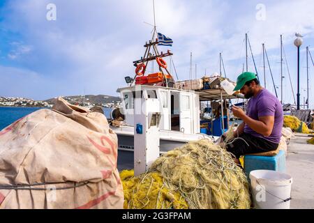 FINIKAS, SIROS, Griechenland, 27.05.2019. Der griechische Fischer repariert seine Nylonfischernetze am Pier im Hafen von Finikas auf der Insel Siros, Kykladen, Griechenland. Stockfoto