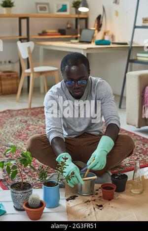 Junger Gärtner, der sich um seine Pflanzen kümmert, während er auf dem Boden im Zimmer sitzt Stockfoto