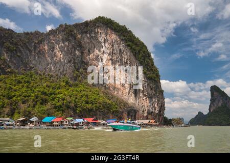 Spektakuläre natürliche Felsformationen und ein Wasserdorf auf Stelzen in der Phang Nga Bay Thailand gebaut. Ein modernes Motorboot bewegt sich im Vordergrund Stockfoto