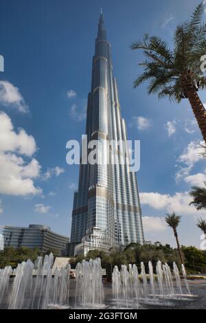 Blick auf das höchste Gebäude der Welt, den Burj Khalifa in Dubai, den Vereinigten Arabischen Emiraten. Palmenumrahmung im Vordergrund und blauer Himmel mit weißen Wolken Stockfoto