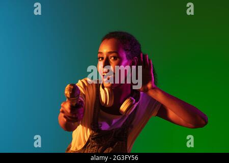 Latino-Sängerin Porträt isoliert auf Studio-Hintergrund in Neonlicht. Schöne weibliche Modell in schwarz tragen mit Mikrofon. Stockfoto