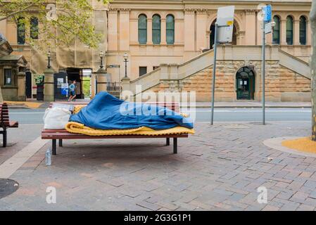 Eine Person, die auf einer Parkbank oben auf dem Martin Place im Zentrum von Sydney, in der Nähe der Reserve Bank und des Landtags, „rauh“ schleicht Stockfoto