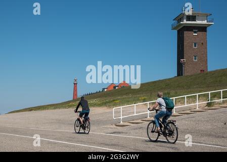 Radfahrer auf dem Deich bei Huisduinen, Den Helder, mit dem Leuchtturm lange Jaap und dem Küstenwachturm im Hintergrund. Hochwertige Fotos Stockfoto