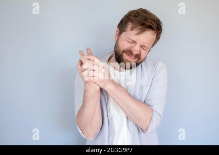 Bärtiger Mann hat starke Schmerzen im Arm, massiert die Wunde Stelle und schließt die Augen im Leiden. Medizinisches Konzept. Stockfoto