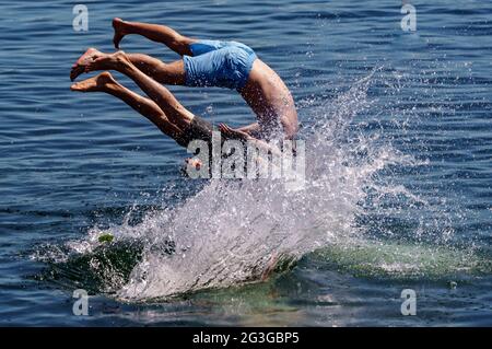 Kiel, Deutschland. Juni 2021. Vier junge Männer springen von einer Schwimmplattform in ein zum Schwimmen gesperrtes Gebiet der Kieler Förde. Auch im Norden beginnt der Sommer heiß. Quelle: Axel Heimken/dpa/Alamy Live News Stockfoto