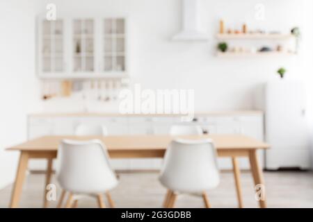 Verschwommenes Kücheninterieur im skandinavischen Stil mit Esstisch und Stühlen aus Holz im Vordergrund Stockfoto