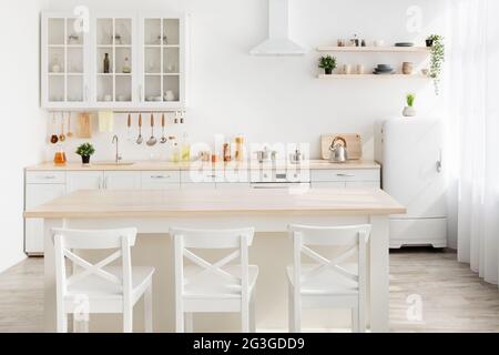 Minimalistischer Stil. Stilvolle Küche aus weißem und braunem Holz. Esstisch, Geschirr und Küchenutensilien auf Regalen Stockfoto