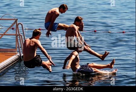 Kiel, Deutschland. Juni 2021. Vier junge Männer springen von einer Schwimmplattform in ein zum Schwimmen gesperrtes Gebiet der Kieler Förde. Auch im Norden beginnt der Sommer heiß. Quelle: Axel Heimken/dpa/Alamy Live News Stockfoto