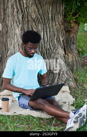 Afrikanischer Geschäftsmann, der online am Laptop arbeitet, während er im Park sitzt Stockfoto